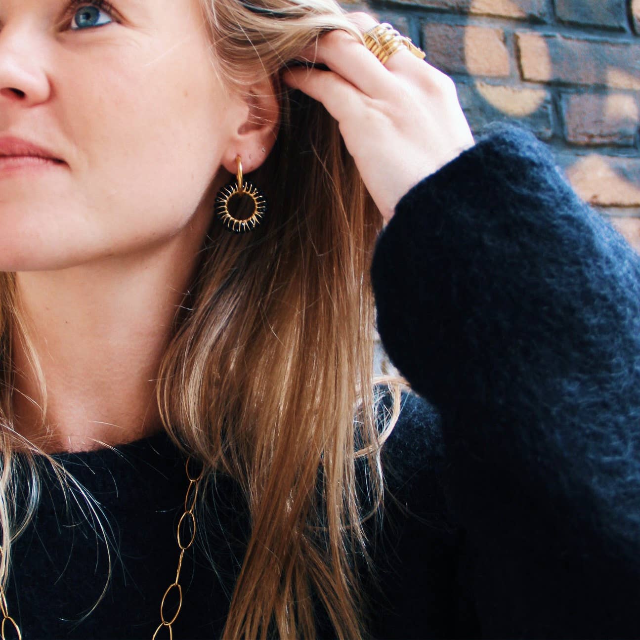 Vrouw met blonde haren draagt Midnight Loop oorbellen van stainless steel. Gouden oorbellen met zwarte details.
