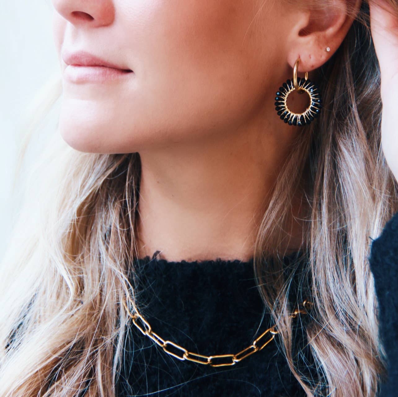 Vrouw met blonde haren draagt Midnight Loop oorbellen van zwart en goudkleurig edelstaal (stainless steel).