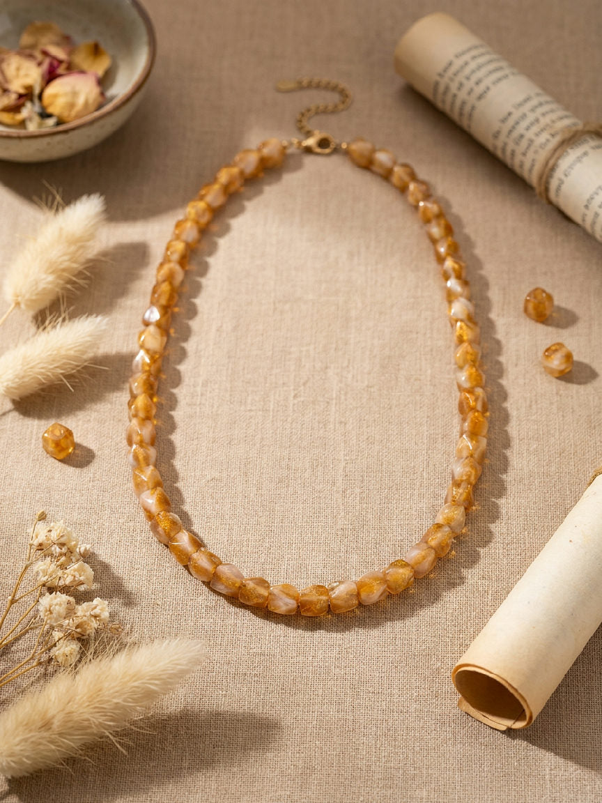 Gedetailleerde close-up van een amberkleurige kralenketting van hars, perfect voor dagelijks gebruik en avondkleding