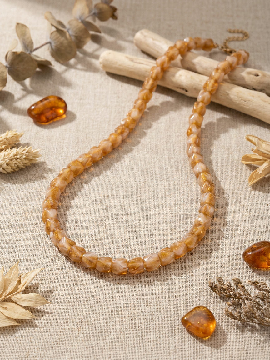 Elegante kralenketting van amberkleurig hars, platgelegd op een neutrale achtergrond, perfect voor elke outfit