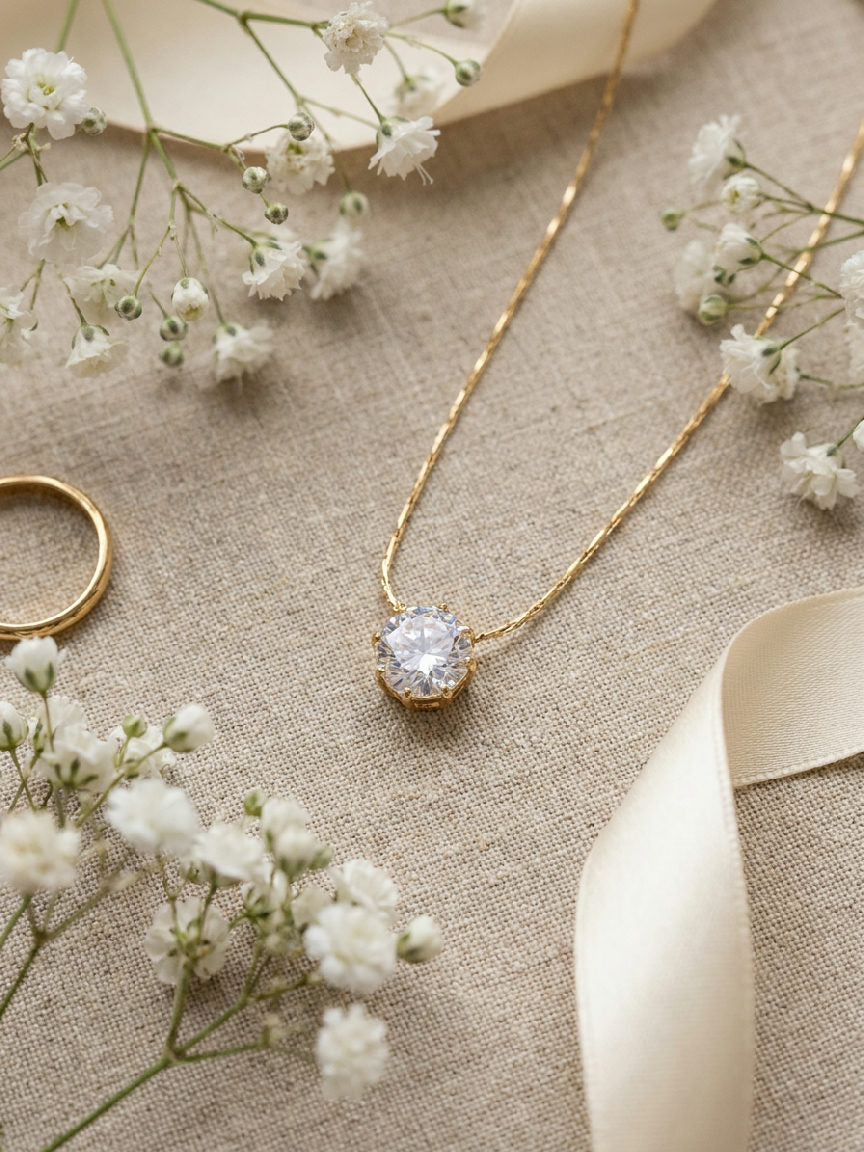 Goudkleurige Aurelia ketting met schitterende zirkoon hanger, gemaakt van stainless steel, op linnen achtergrond met bloemen.