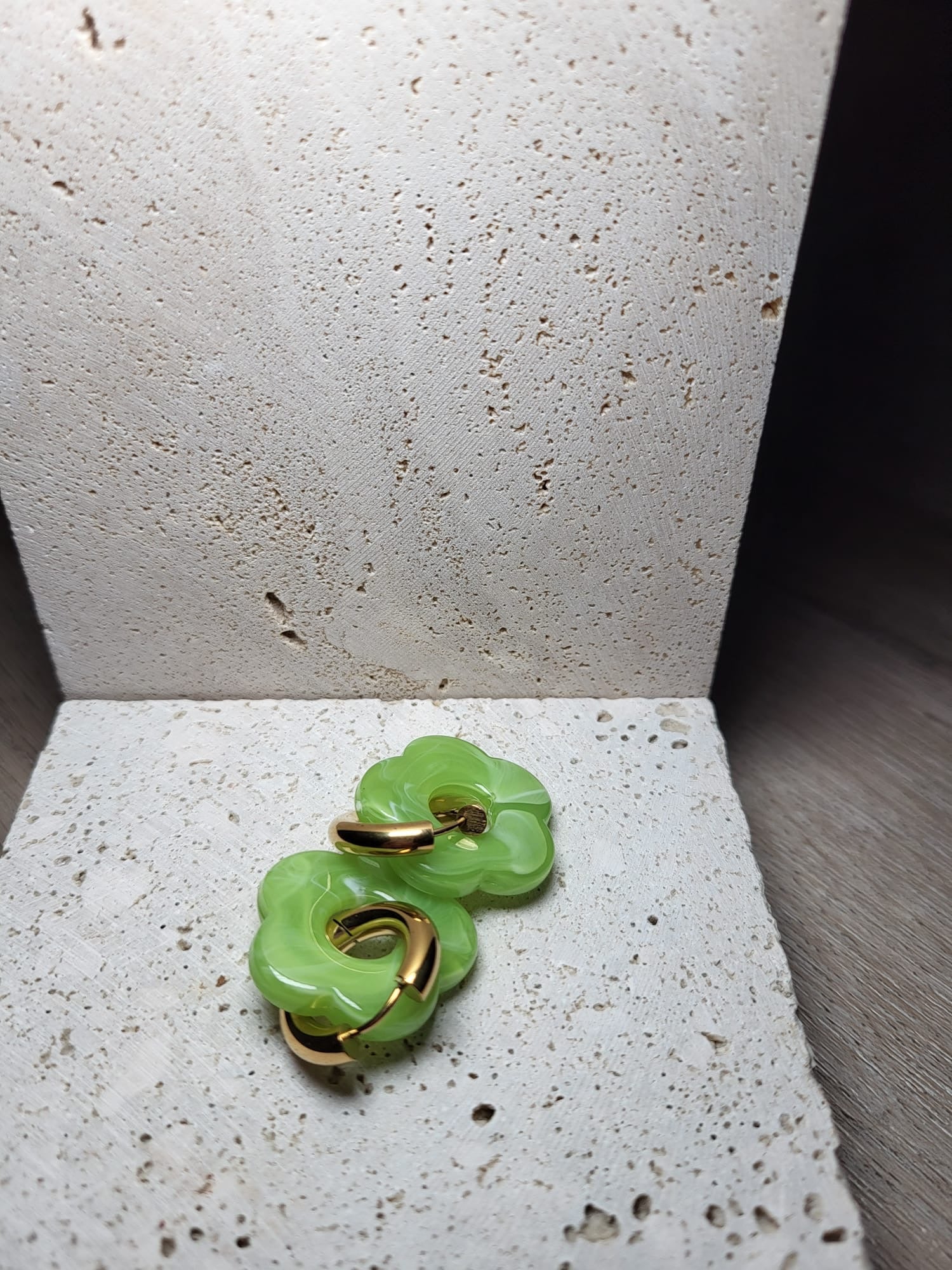 Rosy lichtgroene bloemvormige oorbellen met gouden ronde hangers op een lichte stenen ondergrond