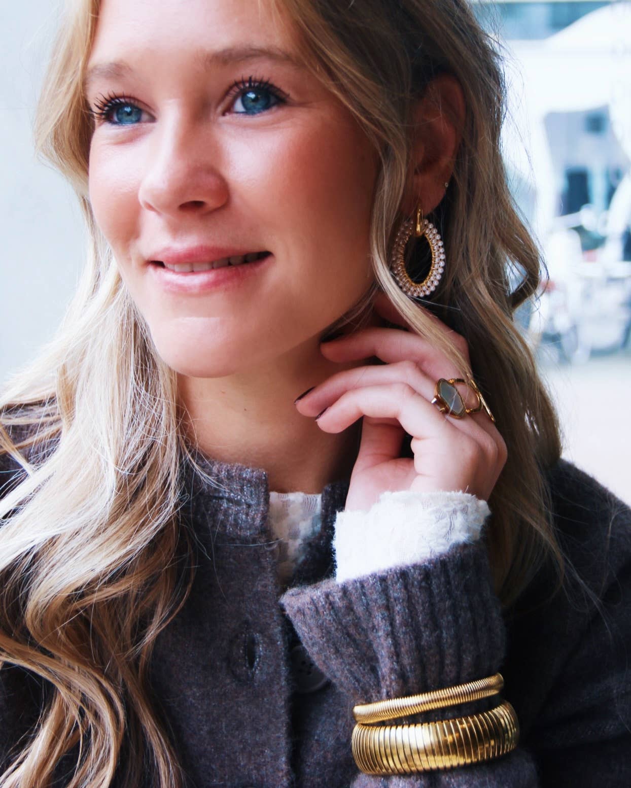 Vrolijke blonde vrouw draagt Pearl Loop oorbellen van stainless steel met parels, ring en gouden armbanden.