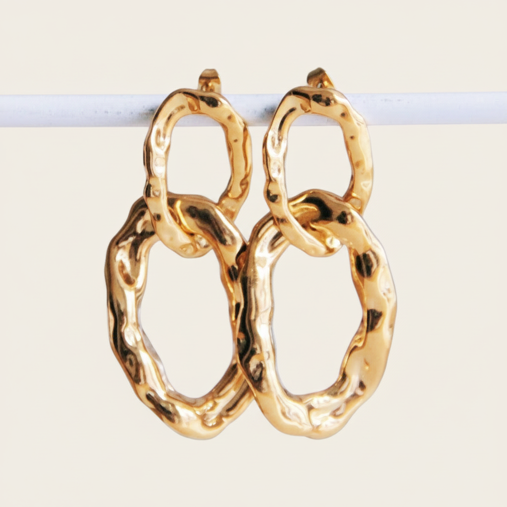 Gouden bold chain oorbellen van roestvrij staal met organische, gehamerde schakels hangend aan een witte staaf.