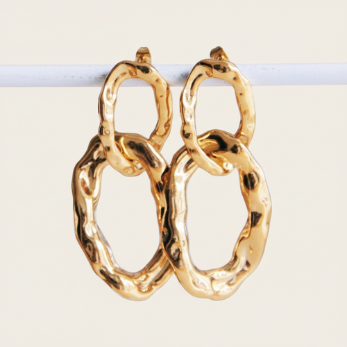 Gouden bold chain oorbellen van roestvrij staal met organische, gehamerde schakels hangend aan een witte staaf.