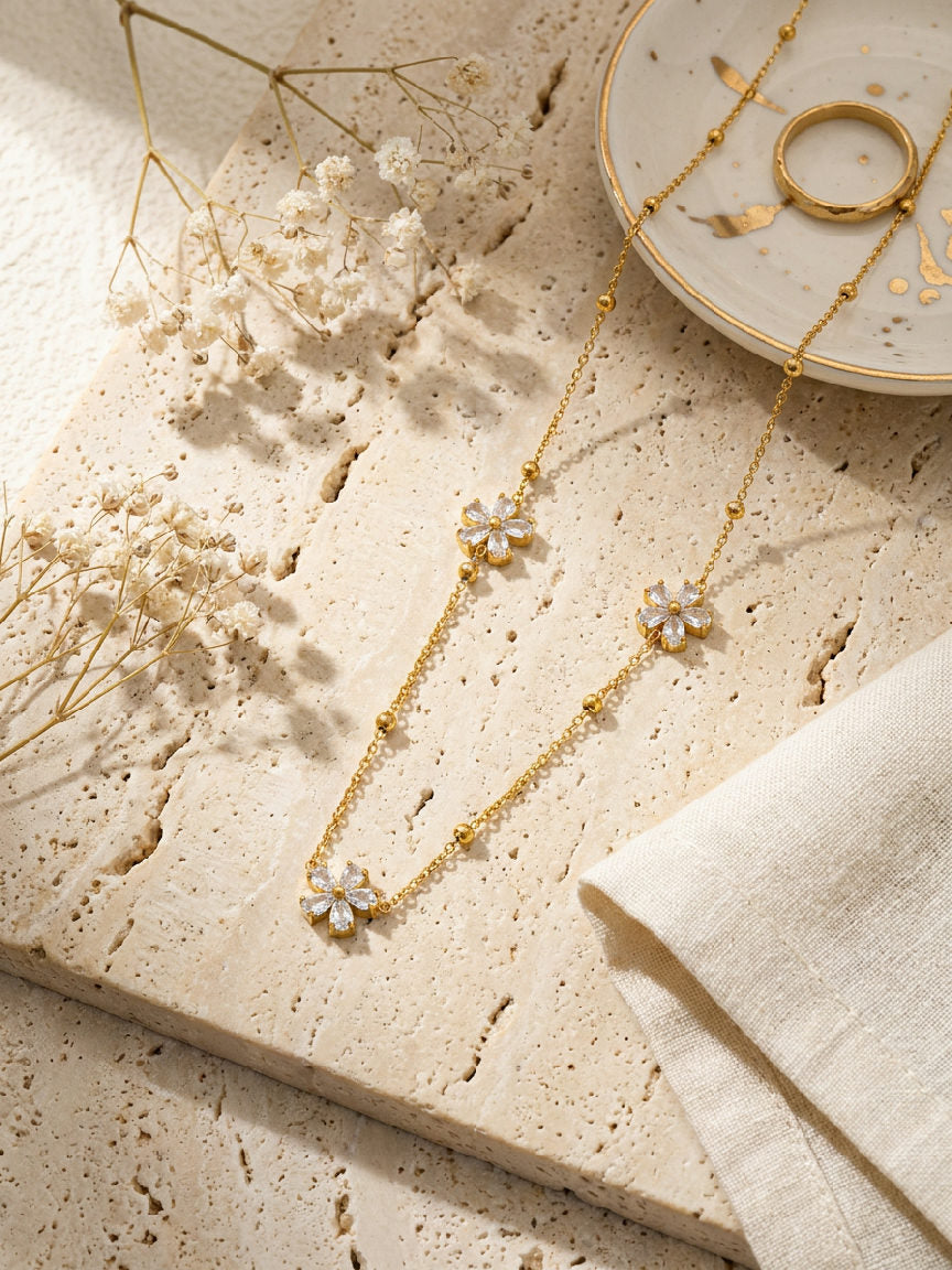 Gouden stainless steel bloemen ketting met zirkonia, op een lichte ondergrond met droogbloemen.