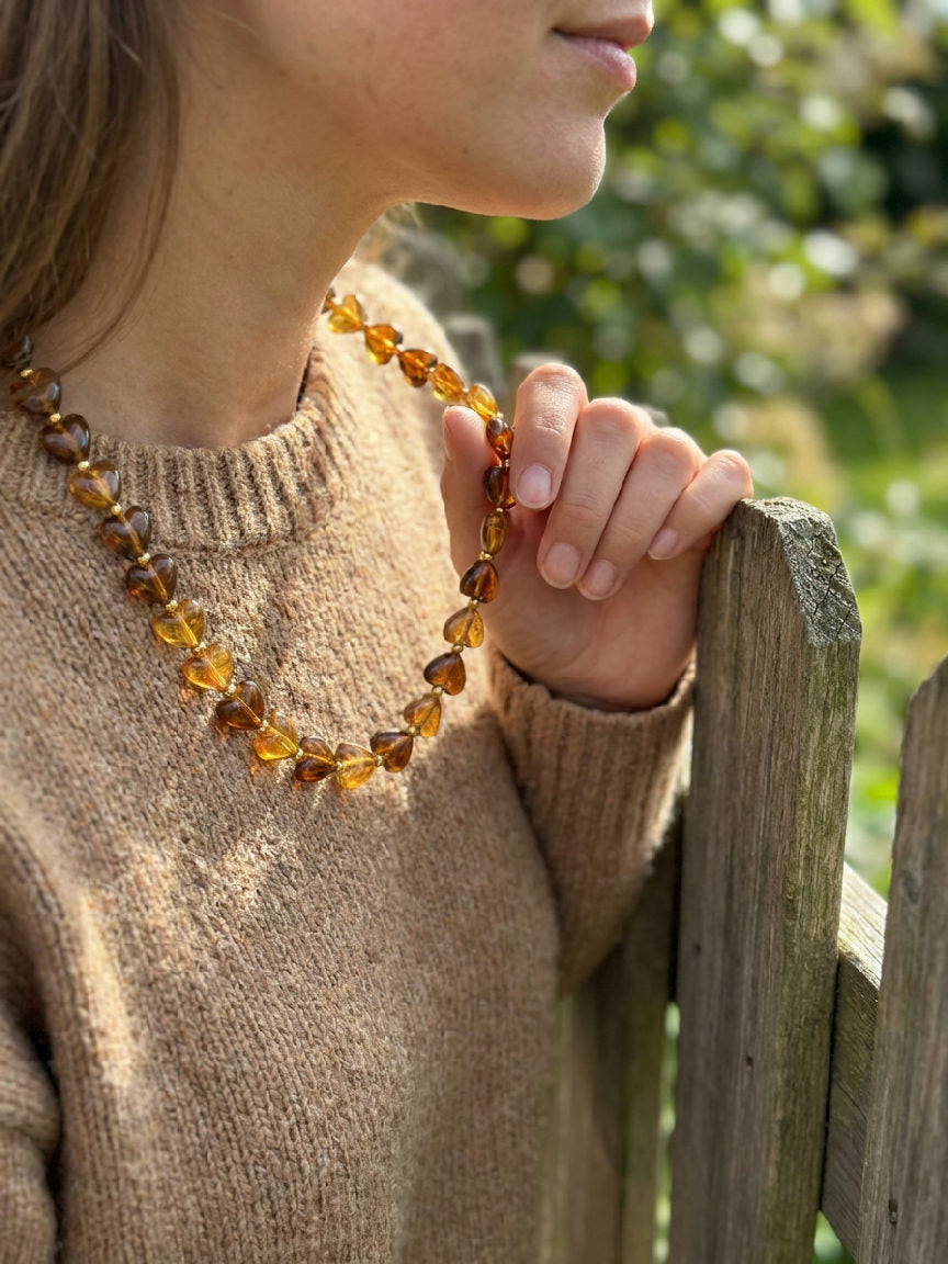 Close-up van een vrouwelijke hals met een gouden Mila ketting met kleine hartjes en een amberkleurige edelsteen