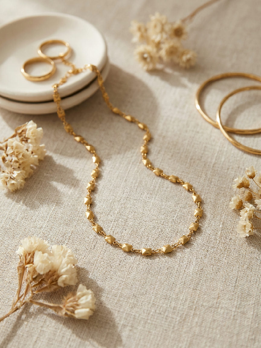 Gouden Nola ketting van roestvrij staal met kleine vierkante schakels op een lichte ondergrond.