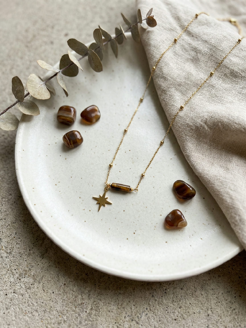 Gouden Solène ketting van stainless steel met sterhanger en tijgeroog kraal op een bord