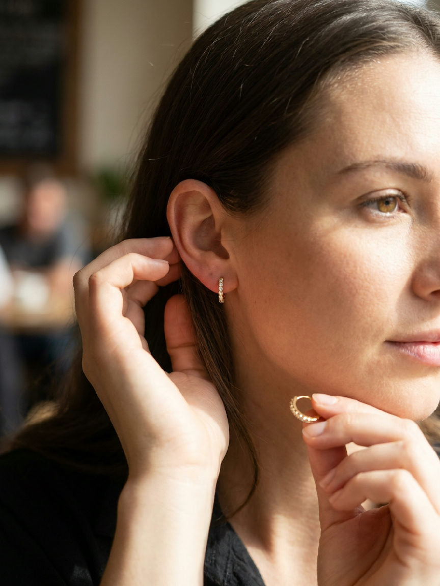 A woman wears small, sparkling 8mm hoop earrings made of stainless steel, adding a subtle shimmer to her ear.