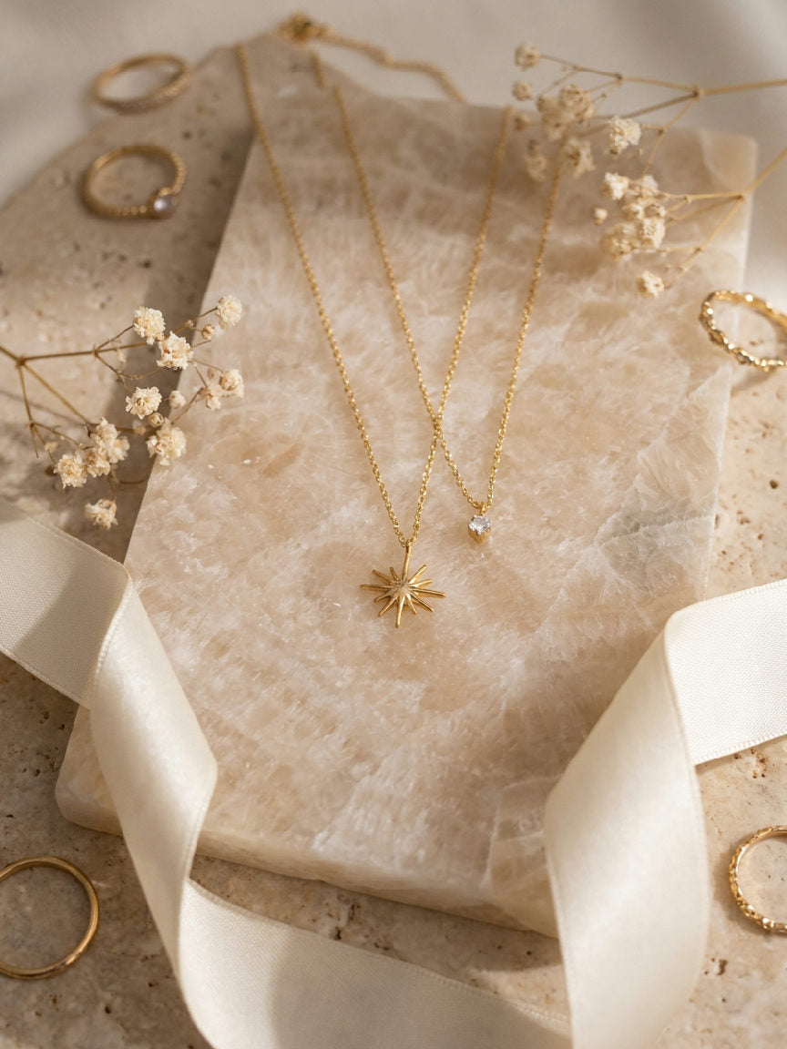 Gouden dubbele ketting van stainless steel met een sterhanger en een hanger met zirkonia steen op marmeren ondergrond