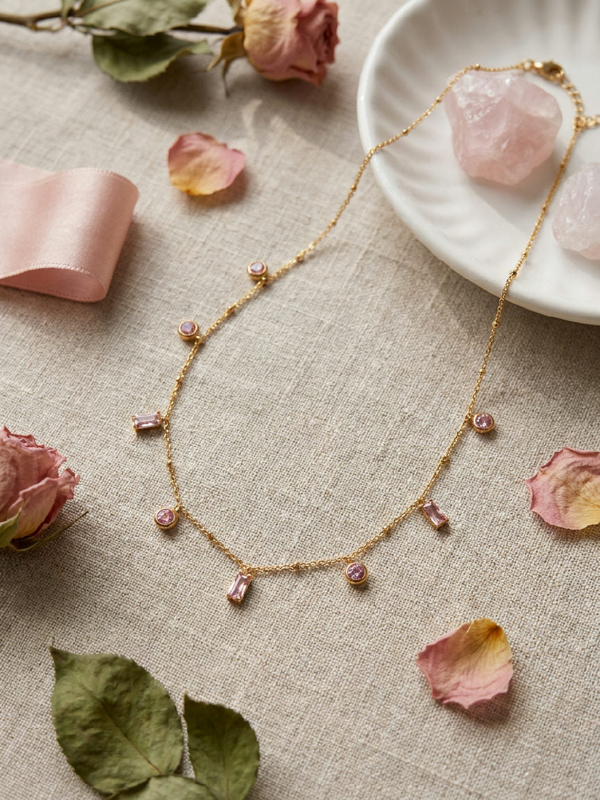 Gouden stainless steel ketting met roze steentjes en rozenkwarts edelstenen op beige linnen, elegante dames sieraden.